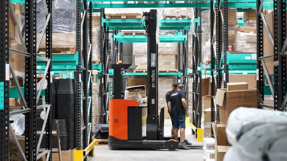 Almacén moderno con estanterías llenas de cajas y trabajador usando escáner